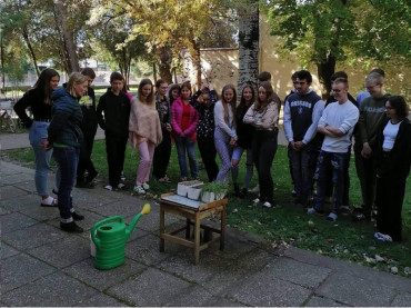 Študenti  na školskom dvore stoje pred demonštračným stolom a čakajú na simuláciu pôdnej erózie a zrážkového javu.
