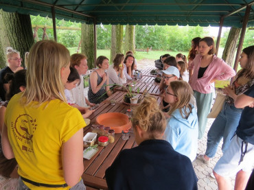A látogatók a terasz asztalainál ülve hallgatják az előadót és nézik a mezőgazdasági termények mintáit.